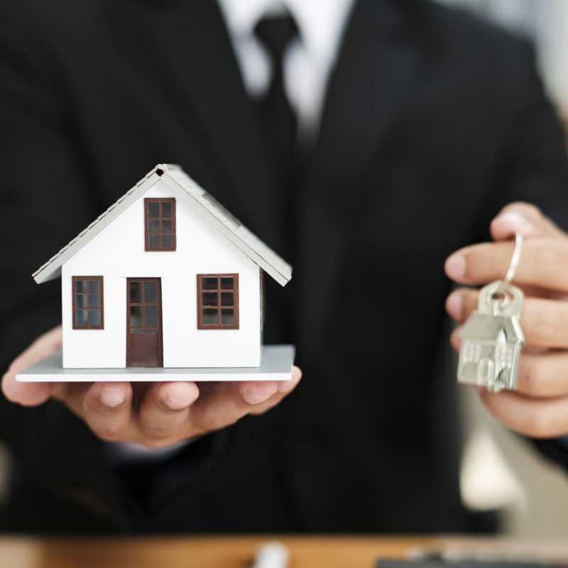 Businessman holding a house model and House Keys.