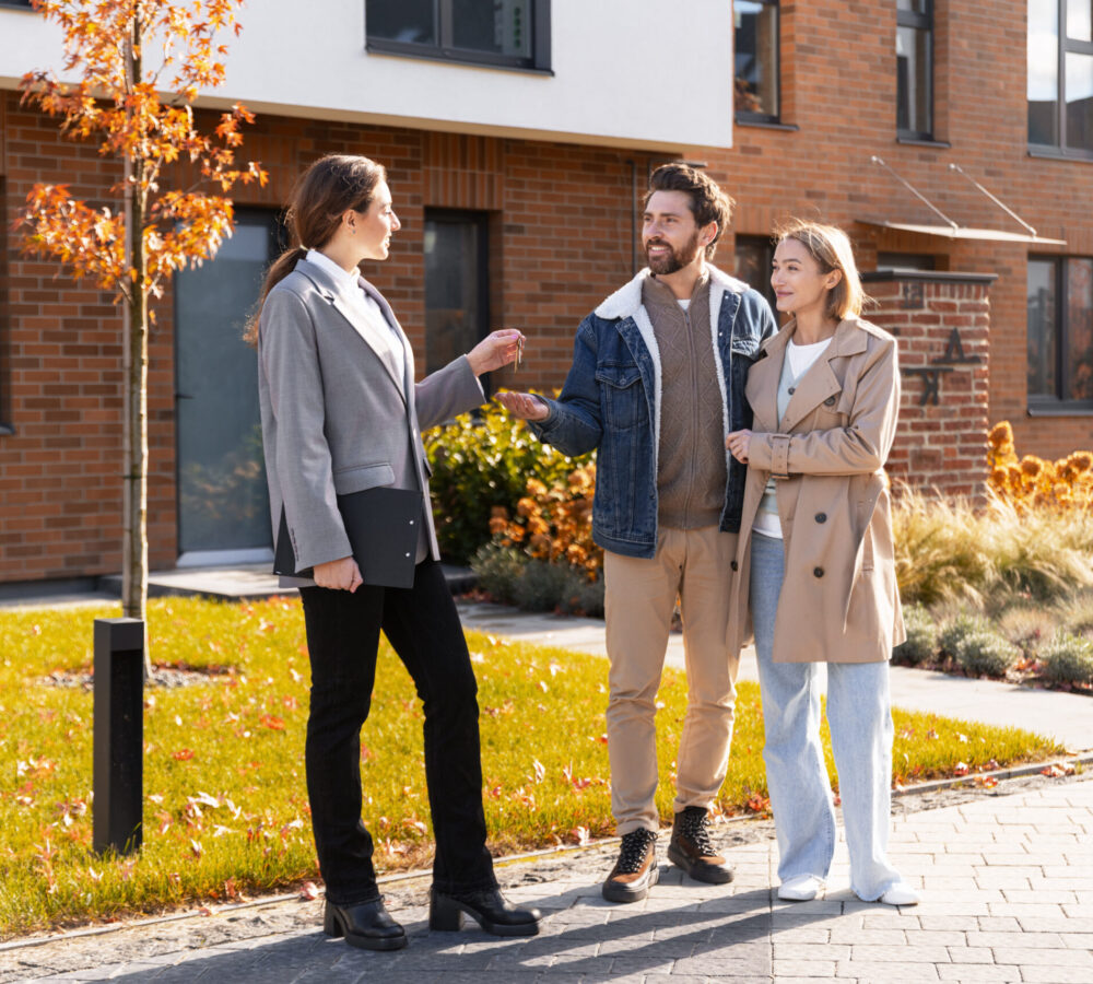Real estate agent handing over house keys to a smiling couple in front of their new home